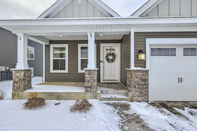 snow covered property entrance featuring board and batten siding, stone siding, a porch, and an attached garage