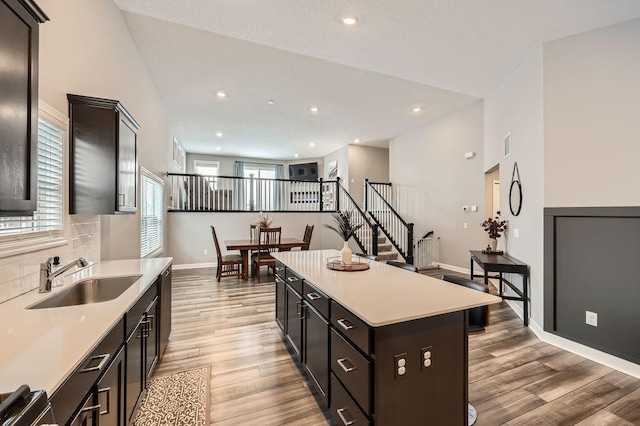 kitchen with tasteful backsplash, light wood-style flooring, a kitchen island, light countertops, and a sink