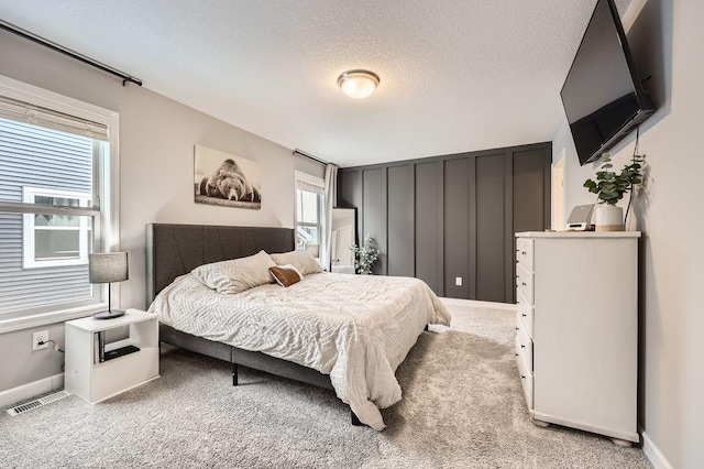 bedroom featuring light carpet, baseboards, visible vents, and a textured ceiling