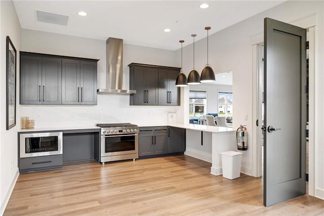 kitchen with light countertops, high end stainless steel range oven, built in microwave, a peninsula, and wall chimney exhaust hood