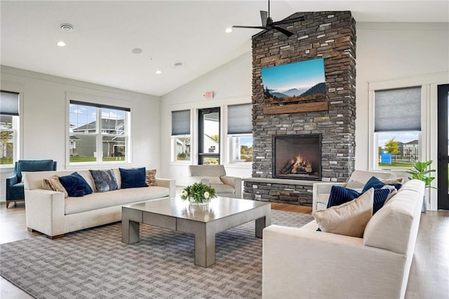 living room with visible vents, high vaulted ceiling, a stone fireplace, and light wood-style flooring