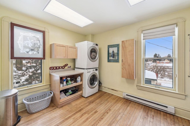washroom with cabinets, stacked washer and clothes dryer, plenty of natural light, and baseboard heating