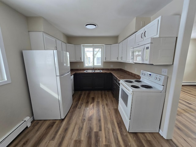 kitchen featuring white appliances, a sink, baseboard heating, dark countertops, and dark wood finished floors