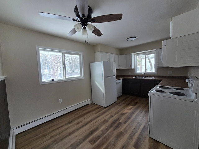 kitchen with a baseboard heating unit, white appliances, a sink, dark countertops, and dark wood finished floors