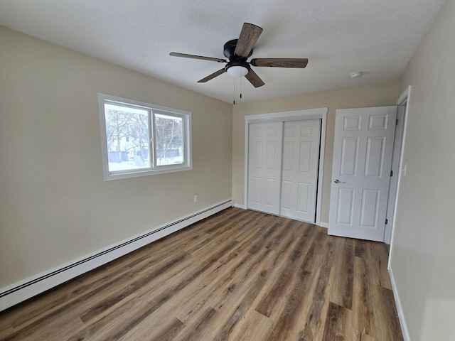 unfurnished bedroom featuring a closet, baseboards, baseboard heating, and wood finished floors