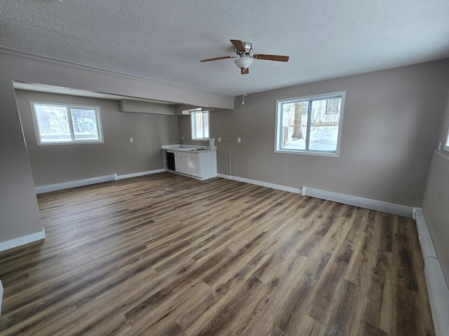 unfurnished living room featuring a wealth of natural light, a textured ceiling, baseboards, and dark wood-style flooring