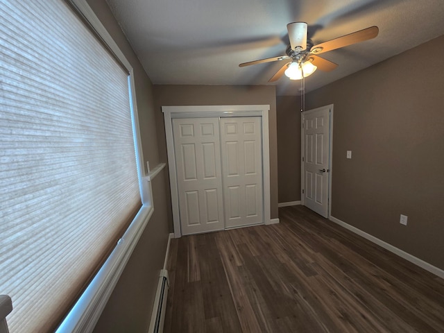 unfurnished bedroom with baseboards, a ceiling fan, dark wood-style flooring, baseboard heating, and a closet