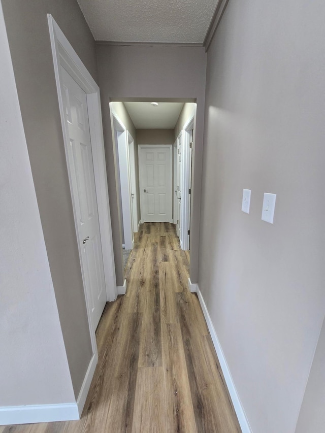 hall with a textured ceiling, baseboards, and wood finished floors