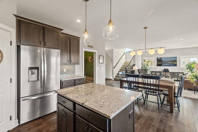 kitchen featuring dark brown cabinetry, decorative backsplash, hanging light fixtures, stainless steel fridge, and dark wood-style flooring