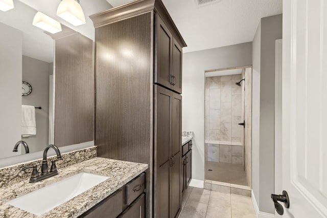 full bath with vanity, baseboards, tile patterned flooring, and tiled shower