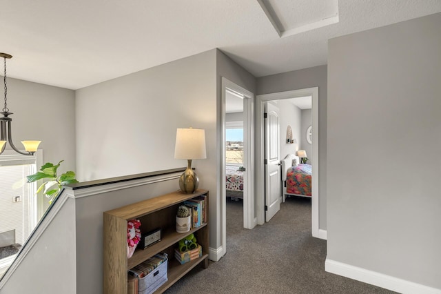 hallway with dark colored carpet, baseboards, an upstairs landing, and a textured ceiling