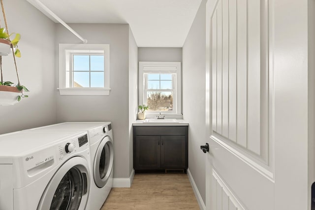 clothes washing area with a sink, washer and dryer, light wood-style floors, baseboards, and laundry area