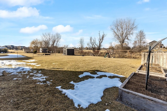 view of yard with a storage unit, fence, a playground, an outdoor structure, and a garden