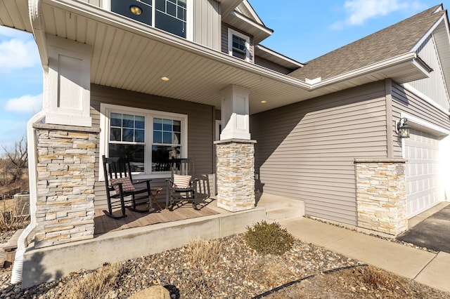 view of exterior entry with stone siding, a porch, an attached garage, and a shingled roof