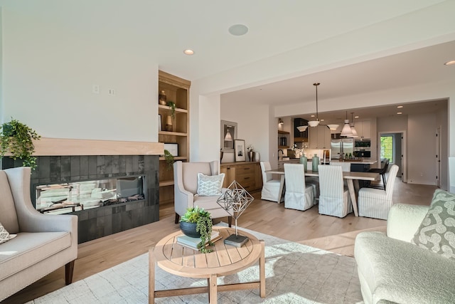 living room with a multi sided fireplace, built in features, and light wood-type flooring