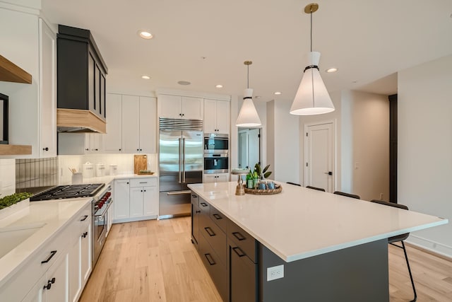 kitchen featuring pendant lighting, white cabinets, high end appliances, a center island, and light wood-type flooring