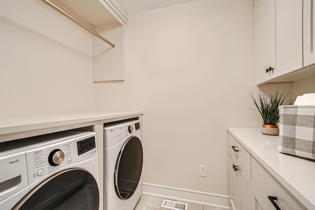 clothes washing area with cabinets and washing machine and clothes dryer