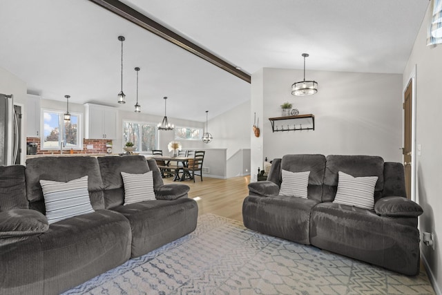 living room featuring sink, light hardwood / wood-style floors, and lofted ceiling with beams