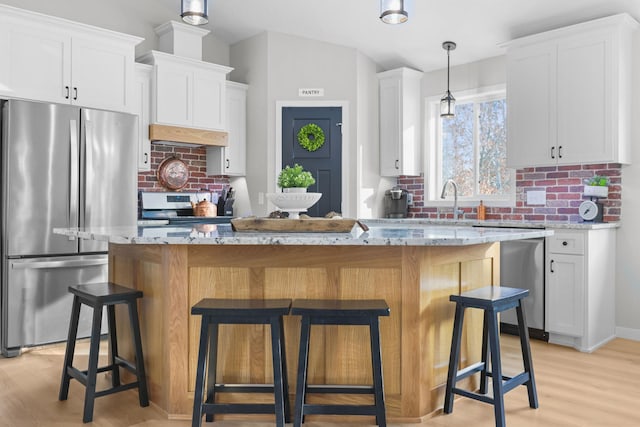 kitchen featuring white cabinetry, decorative light fixtures, light stone countertops, backsplash, and appliances with stainless steel finishes