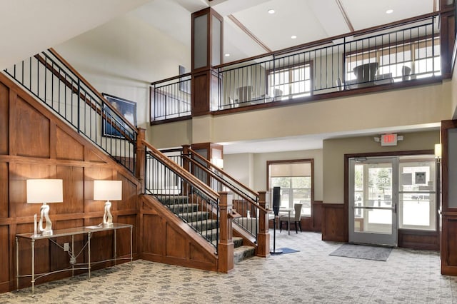 staircase with wooden walls, a wainscoted wall, a high ceiling, carpet flooring, and recessed lighting