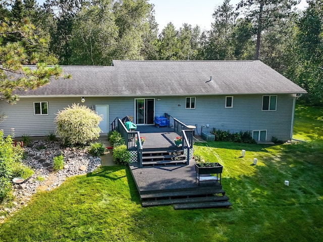 back of property featuring roof with shingles, a deck, and a yard