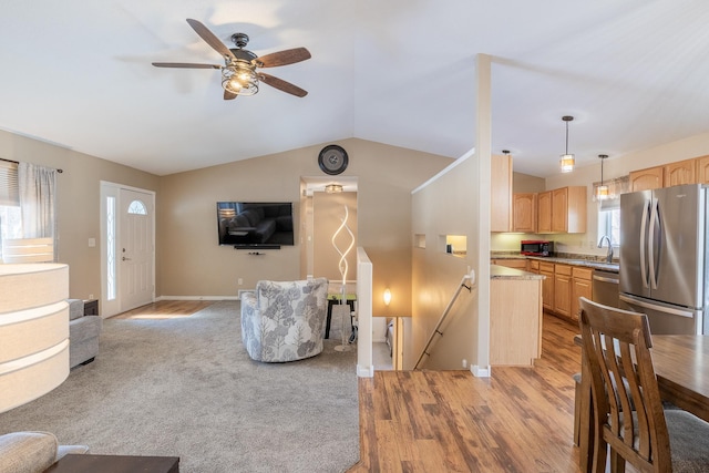 living area featuring light wood-style floors, baseboards, vaulted ceiling, and a ceiling fan