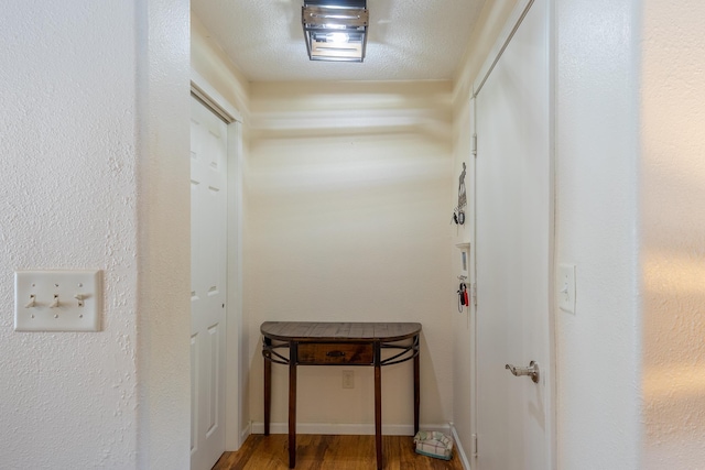 hallway with a textured ceiling, wood finished floors, and baseboards