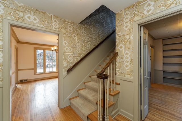 stairs with wallpapered walls, baseboards, visible vents, wood finished floors, and crown molding