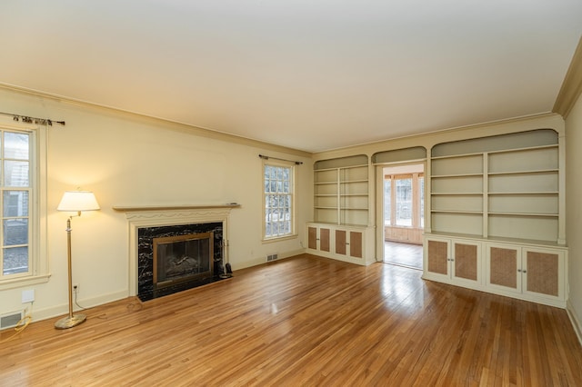 unfurnished living room featuring ornamental molding, a fireplace, wood finished floors, and visible vents