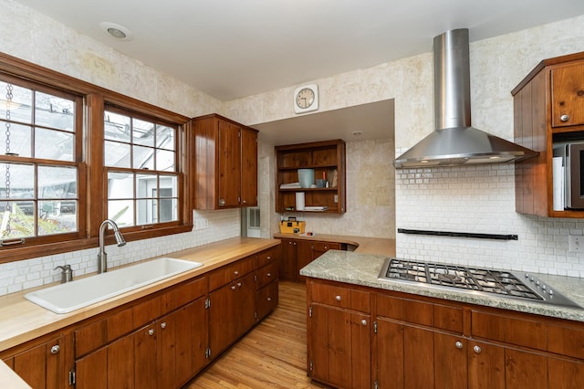 kitchen featuring a sink, light countertops, wall chimney range hood, light wood finished floors, and stainless steel gas stovetop