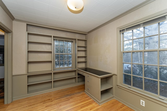 unfurnished office with ornamental molding, light wood finished floors, and built in desk