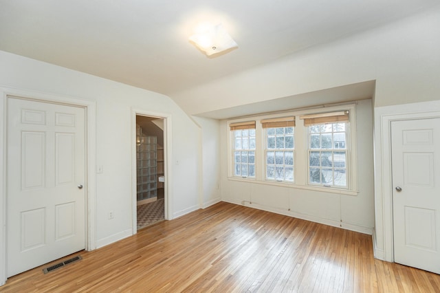 unfurnished bedroom with baseboards, visible vents, ensuite bath, vaulted ceiling, and light wood-style floors