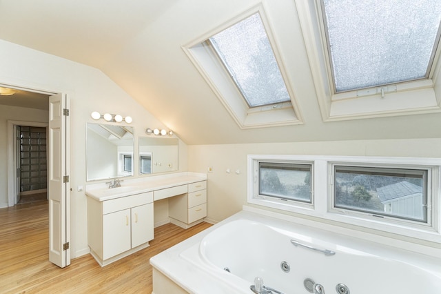 full bath with a whirlpool tub, vaulted ceiling with skylight, wood finished floors, and vanity