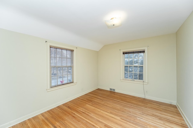 spare room with vaulted ceiling, light wood-type flooring, visible vents, and baseboards