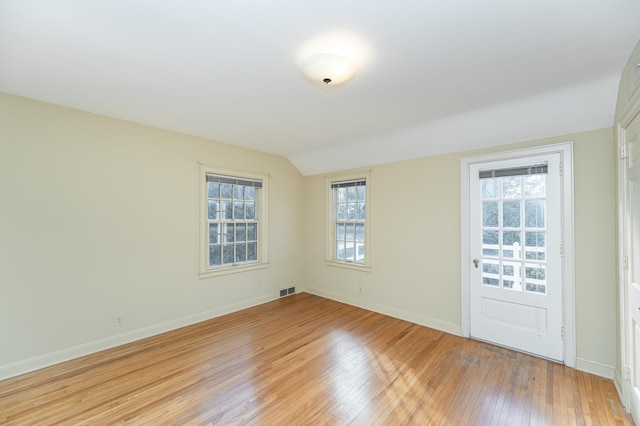 empty room with baseboards, lofted ceiling, visible vents, and light wood-style floors