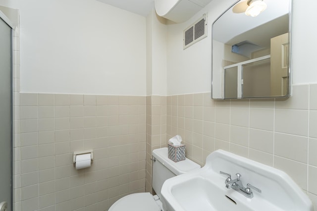 full bathroom with tile walls, visible vents, toilet, a stall shower, and wainscoting