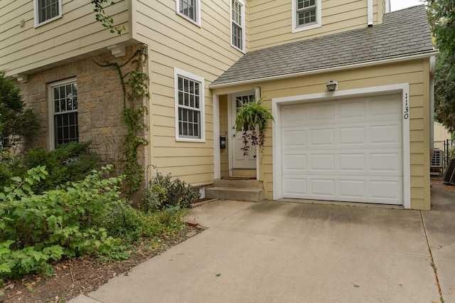 doorway to property with a garage, driveway, a shingled roof, and stone siding