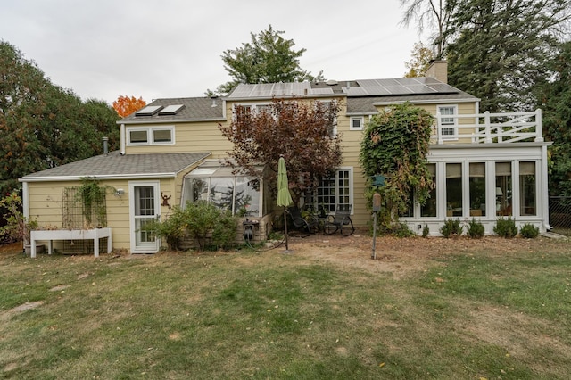 back of property featuring solar panels, a yard, roof with shingles, and a chimney