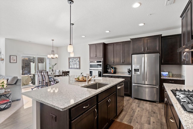 kitchen featuring appliances with stainless steel finishes, sink, hanging light fixtures, dark brown cabinets, and a kitchen island with sink