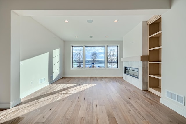 unfurnished living room with a tiled fireplace and light wood-type flooring