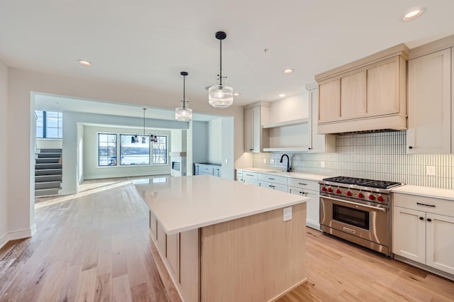 kitchen with sink, hanging light fixtures, a center island, tasteful backsplash, and designer stove