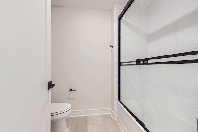 bathroom featuring toilet and shower / bath combination with glass door