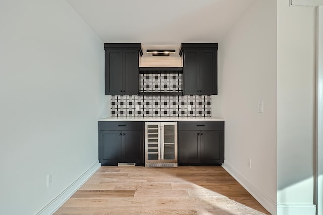 bar with tasteful backsplash, beverage cooler, and light hardwood / wood-style flooring