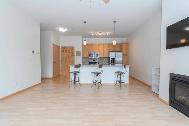 kitchen with a breakfast bar area, hanging light fixtures, light wood-type flooring, appliances with stainless steel finishes, and light stone countertops