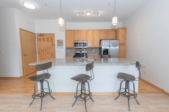 kitchen featuring stainless steel appliances, a kitchen island with sink, sink, and hanging light fixtures