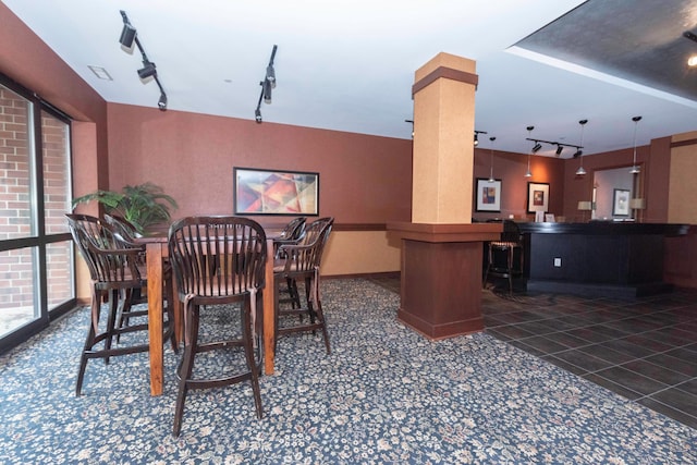 dining room with dark tile patterned floors, bar, rail lighting, and ornate columns