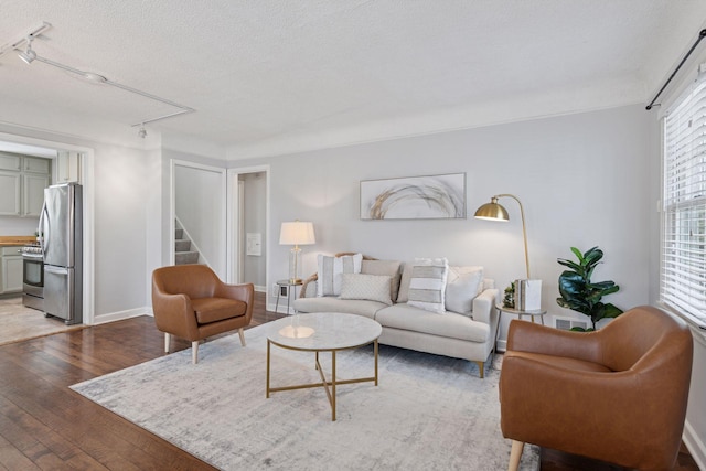 living area featuring baseboards, attic access, stairs, light wood-style floors, and a textured ceiling