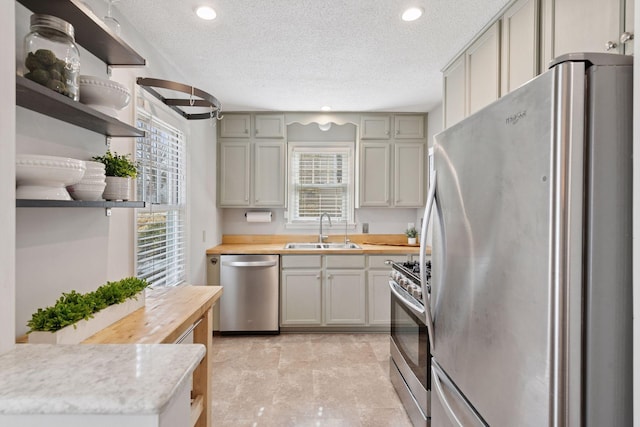 kitchen with open shelves, a sink, butcher block countertops, stainless steel appliances, and a textured ceiling