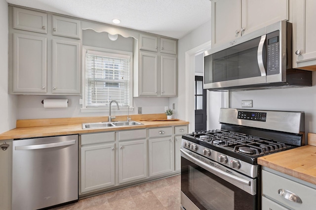 kitchen with a sink, butcher block counters, a textured ceiling, and stainless steel appliances