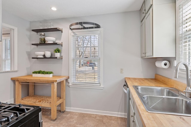 kitchen featuring a wealth of natural light, butcher block countertops, baseboards, and a sink